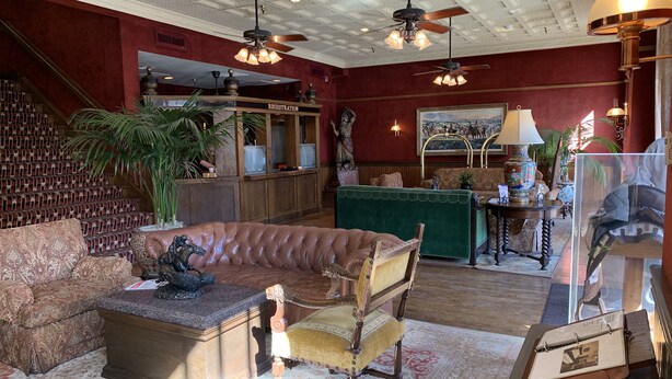 A spacious lobby with a registration desk, a leather sofa, a vintage armchair, and a green sofa. - Stockyards Hotel (Fort Worth)