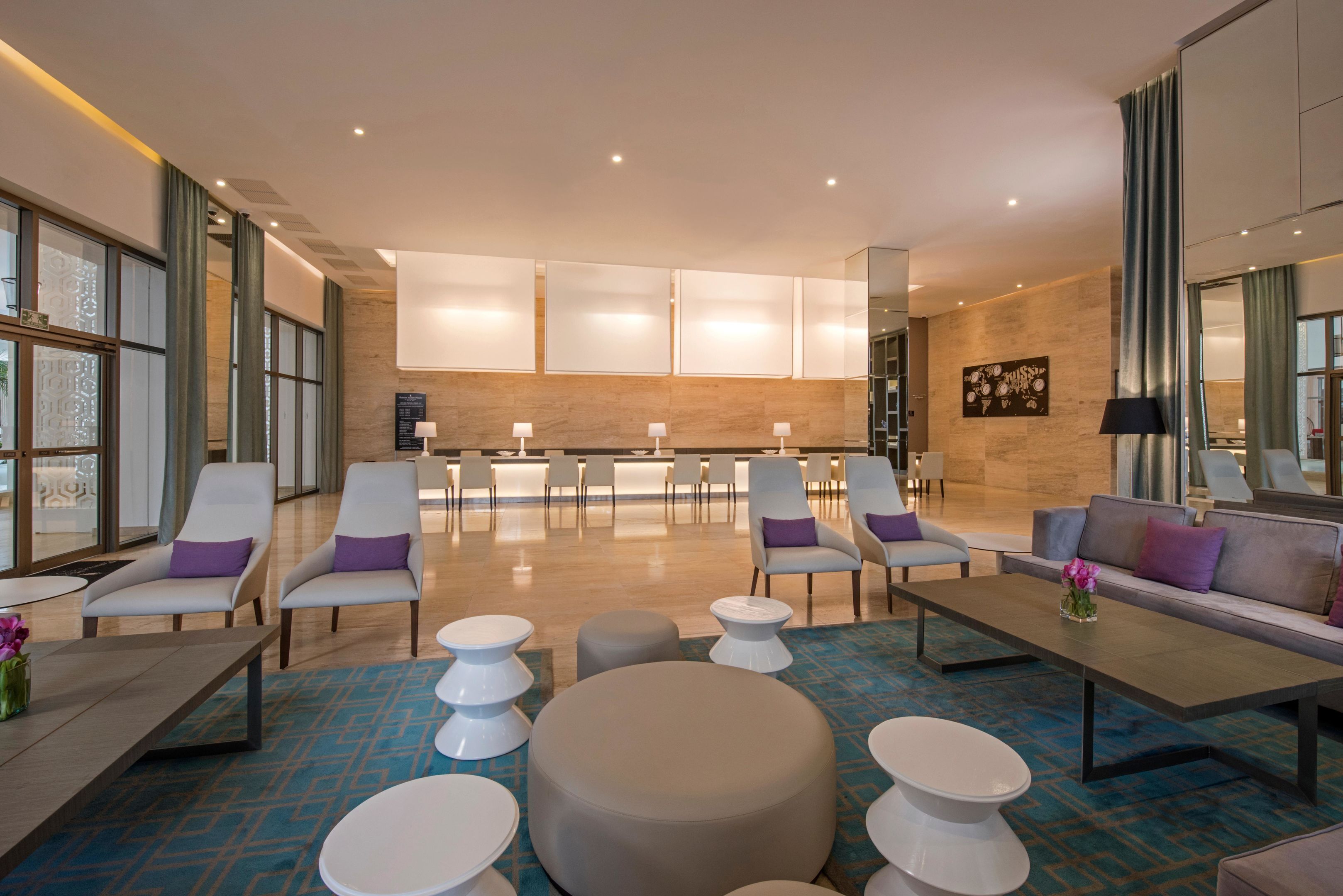 A modern lobby with a central seating area, a reception desk, and a large window with curtains.