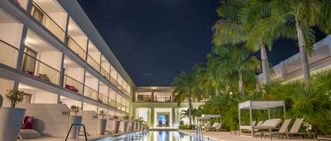 A pool area with a clear view of the pool, lounge chairs, and palm trees.