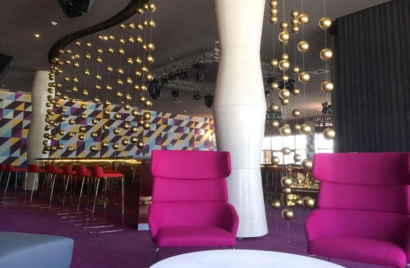 A modern interior with vibrant seating, geometric wall patterns, and hanging spherical decorations. - Platinum Yucatan Princess Adults Only - All Inclusive  (Playa del Carmen)