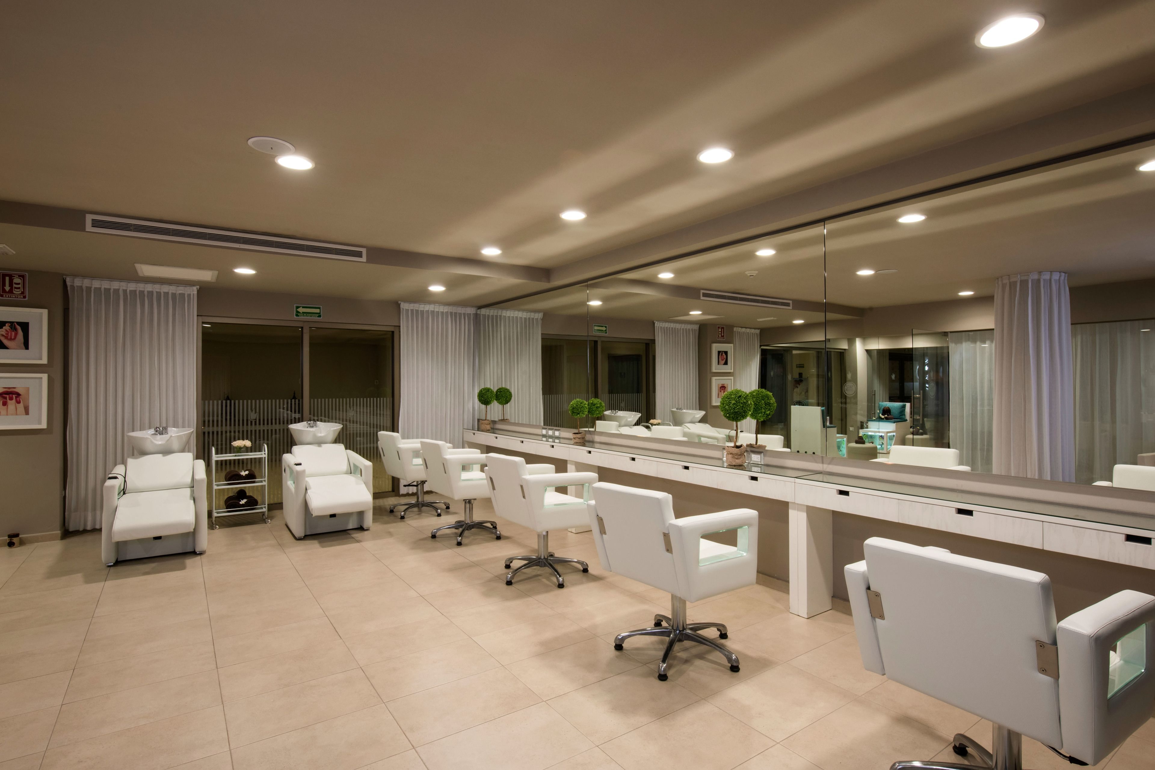 Ein zeitgemäßer Friseursalon mit weißen Stühlen, einem großen Spiegel und einem sauberen Fliesenboden.