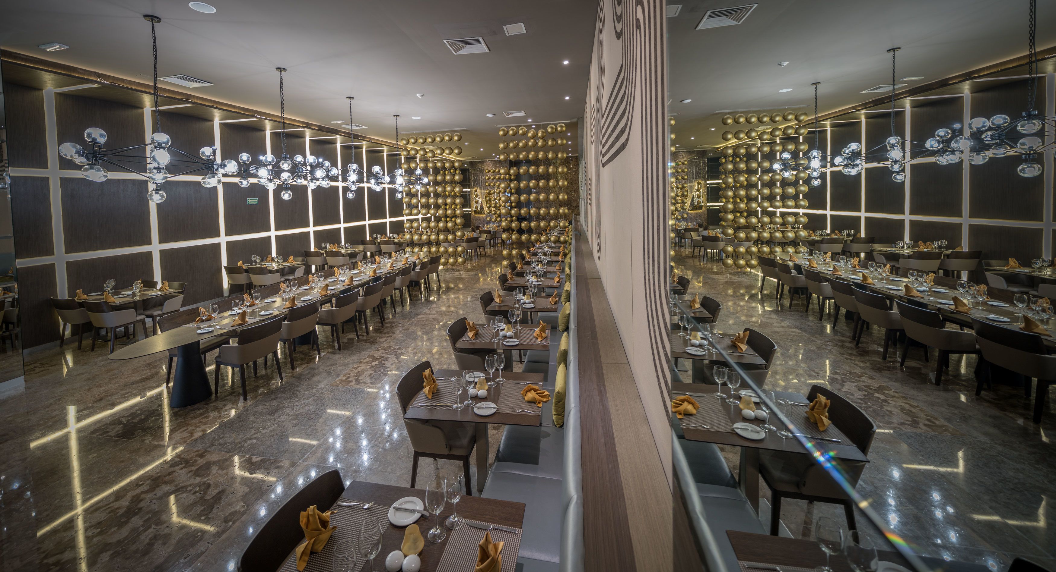 A spacious restaurant with multiple dining tables and chairs, a polished marble floor, and a modern chandelier.