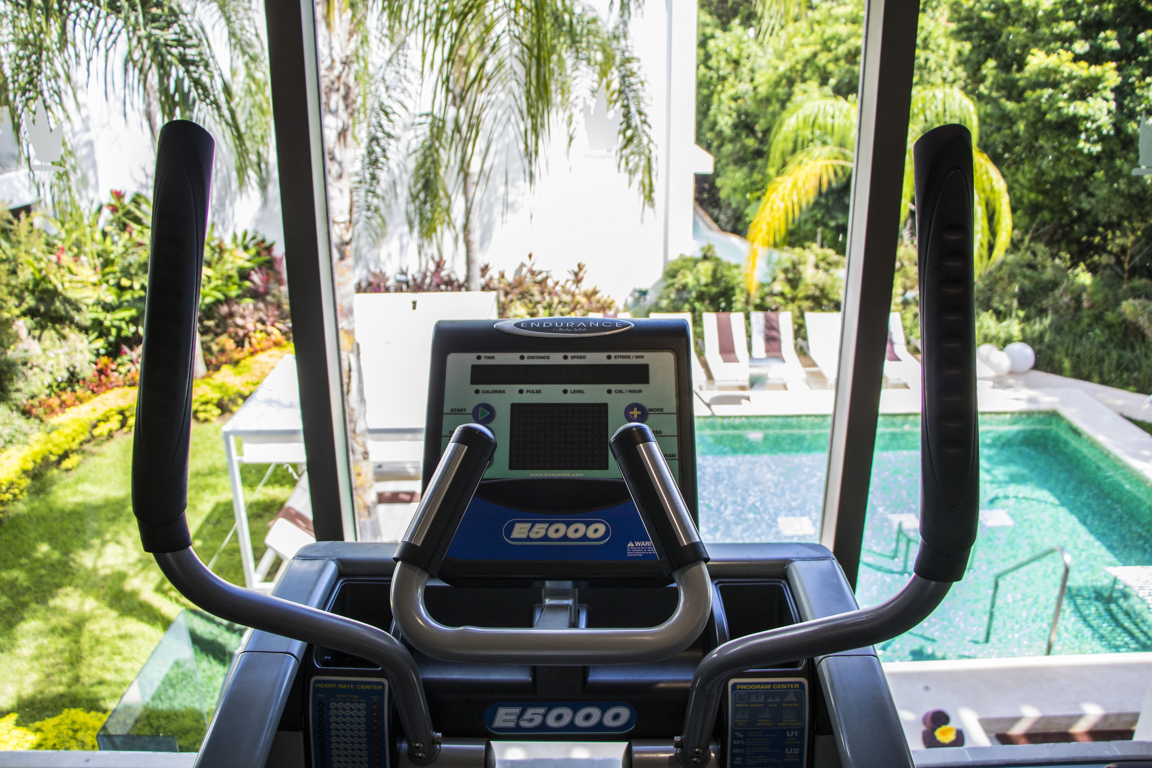 An indoor exercise machine with a digital display, positioned near a window overlooking a pool and garden.