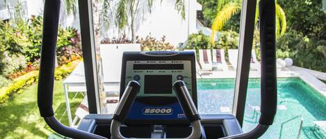 An indoor exercise machine with a digital display, positioned near a window overlooking a pool and garden.