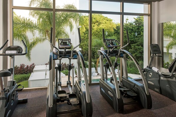 Un gimnasio con cintas de correr y elípticas, ventanas amplias y vistas al exterior con zonas verdes.