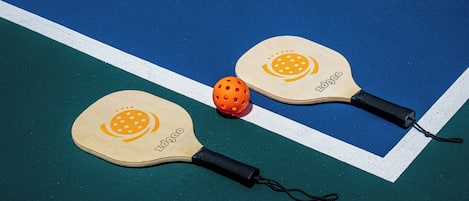 Two paddleball paddles and a ball on a blue and green court.