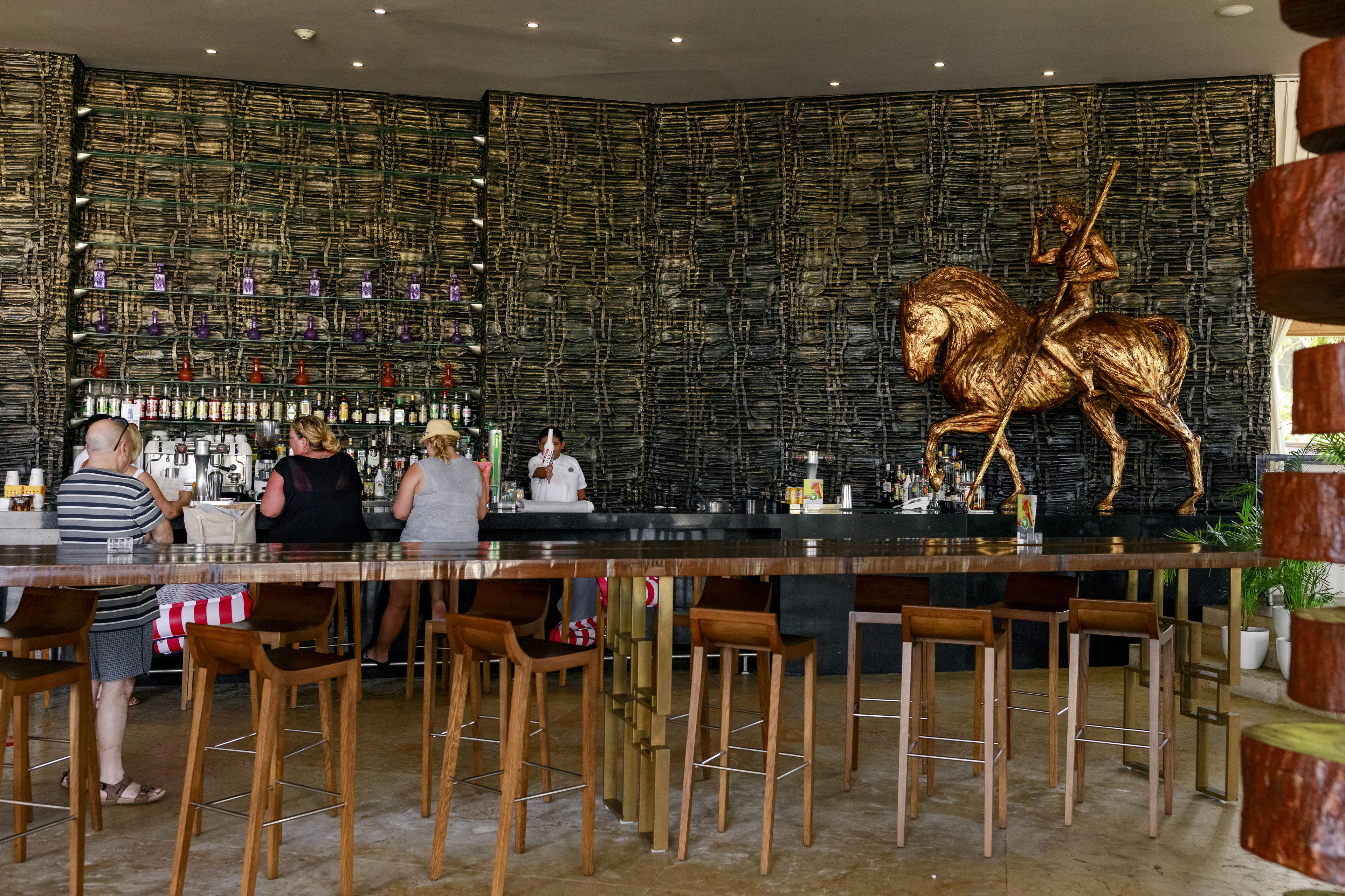 Zona de bar con un diseño de pared único, taburetes de madera y una gran escultura de bronce de un caballo.