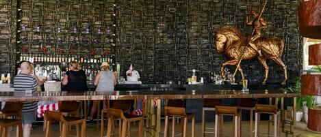Zona de bar con un diseño de pared único, taburetes de madera y una gran escultura de bronce de un caballo.