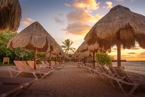 Une plage bordée de parasols en chaume et de chaises longues alignées le long du rivage.