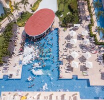 An aerial view of a resort with a large central pool surrounded by lounge areas and palm trees.