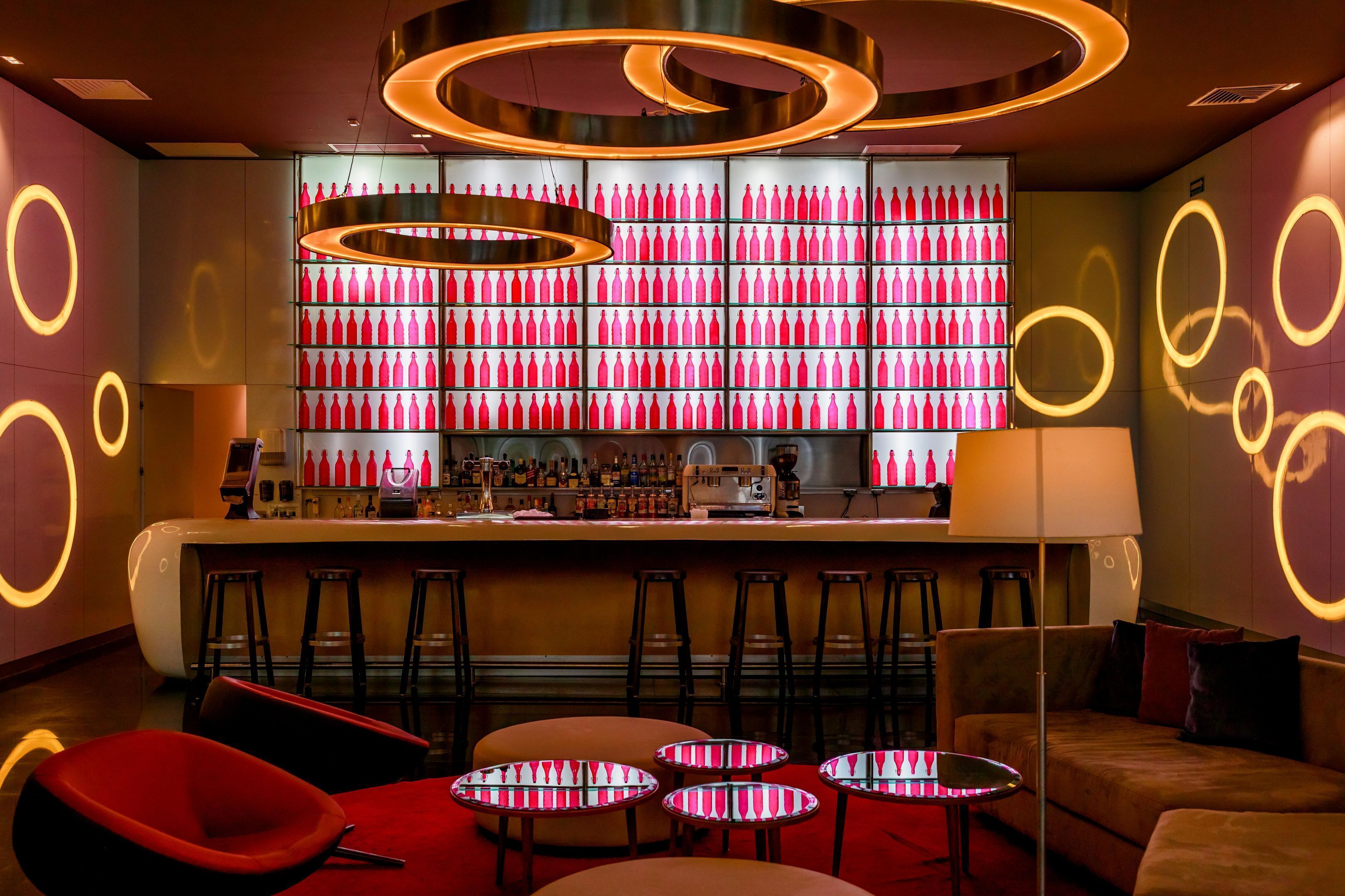 Un espace bar aux couleurs rouge et rose, avec de nombreux tabourets et un comptoir.