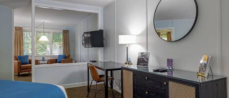 Ein Hotelzimmer mit Bett, Schreibtisch mit Stuhl, Fernseher, Lampe und einem großen Spiegel.