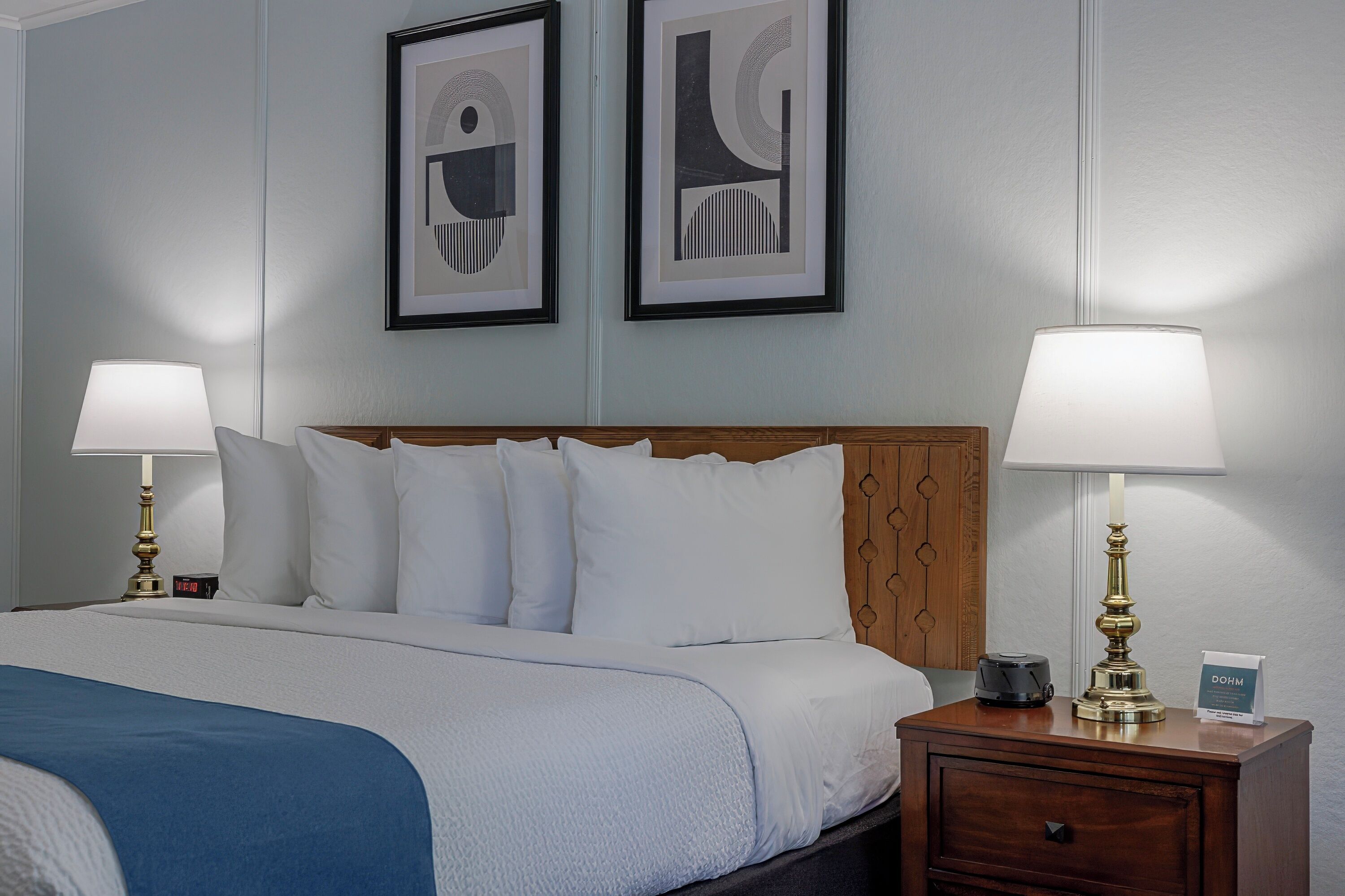 A neatly made bed with white linens, a blue throw blanket, two bedside tables with lamps, and a wooden headboard.
