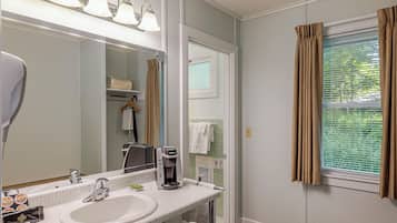 A bathroom with a sink, mirror, and coffee maker. There is a towel rack and a window with curtains.