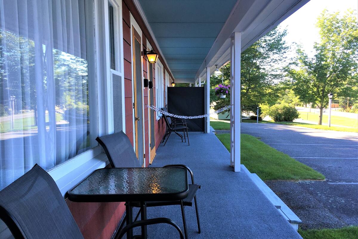 A covered porch with a table and chairs, a hanging flower pot, and a chain-link fence.