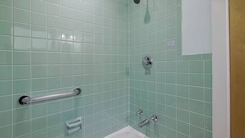 Un baño con azulejos verdes, una bañera blanca, un cabezal de ducha y un asidero.