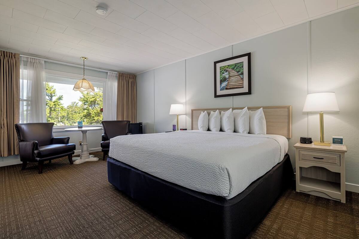 A hotel room with a large bed, two bedside tables, a chair, a desk, and a window with curtains.