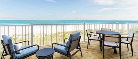 A wooden deck with outdoor furniture, including two chairs and a table, overlooking a beach.