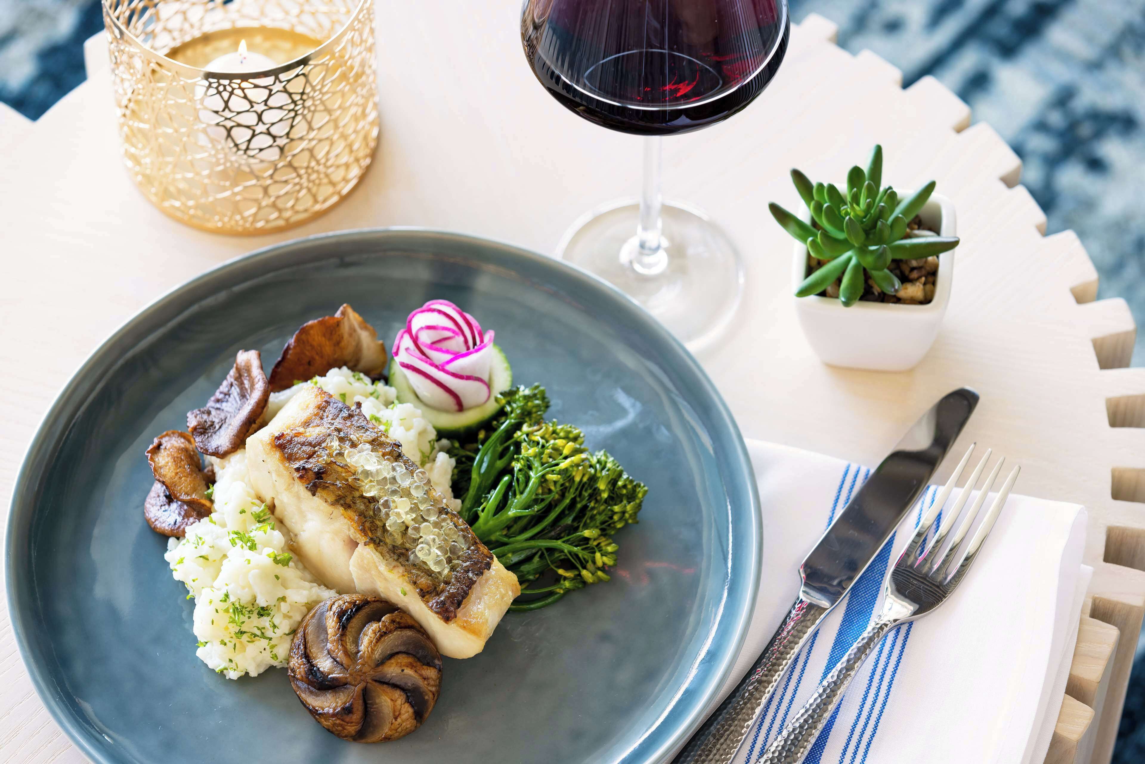 A plate of food with a fish fillet, mushrooms, and vegetables, accompanied by a glass of red wine and a candle.