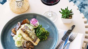 Un plato de comida con un filete de pescado, champiñones y verduras, acompañado de una copa de vino tinto y una vela.