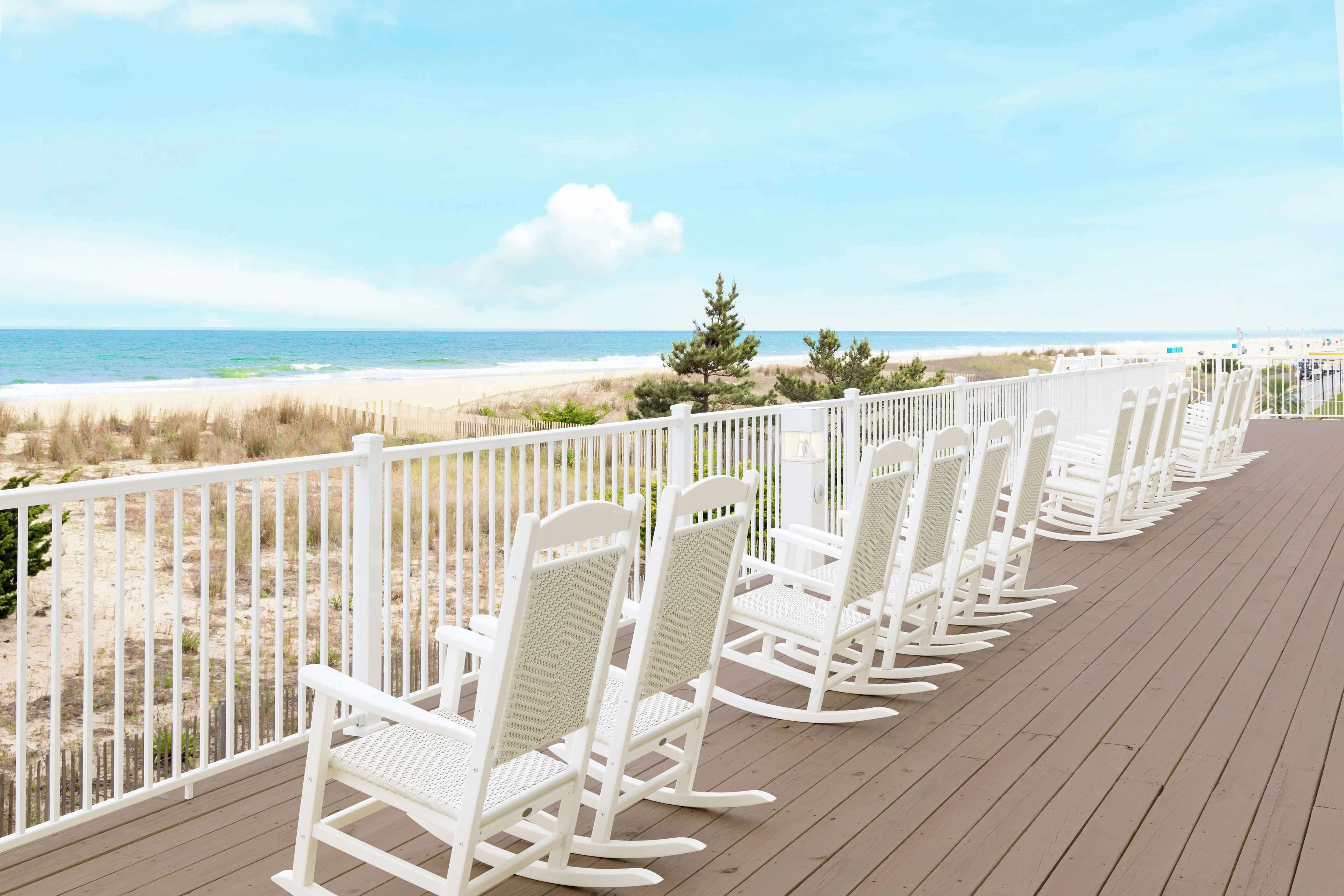 Una terraza de madera con mecedoras blancas orientadas hacia la playa.