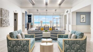 Un salón amplio con vista a la playa, que incluye dos sofás, una mesa de centro y una estantería.