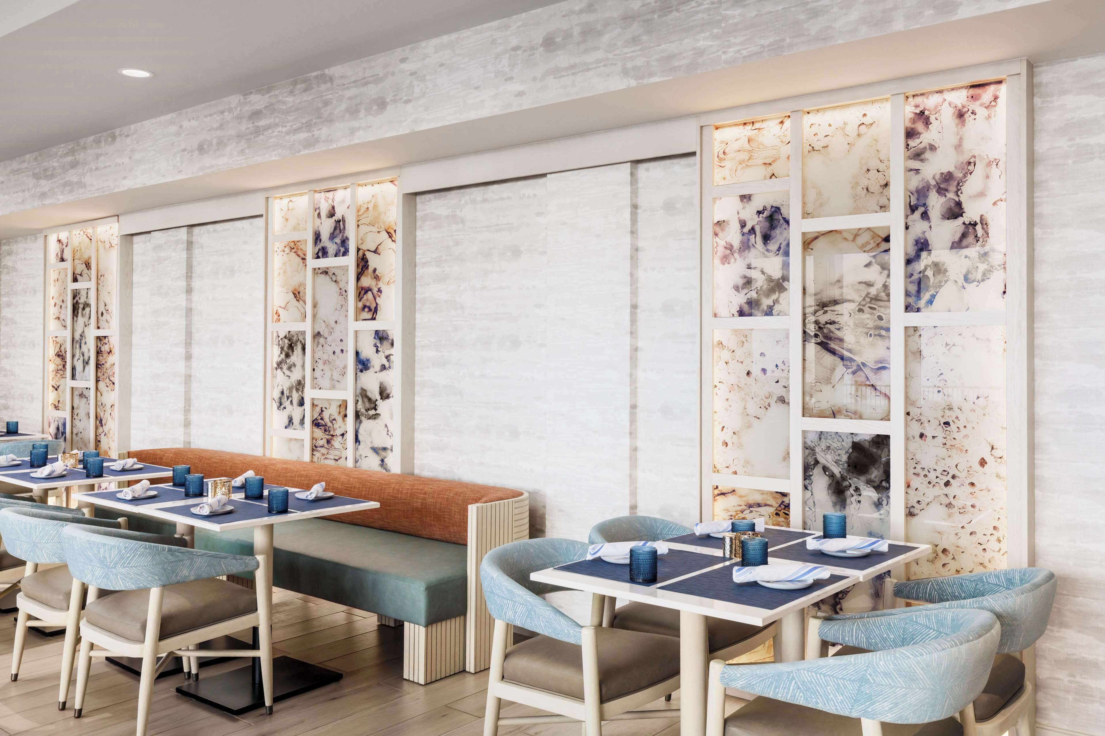 Un espace repas moderne, avec des banquettes et des tables, chacune agrémentée de serviettes bleues et d’assiettes blanches.