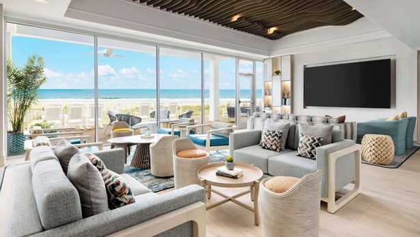 Un amplio salón con una ventana grande con vistas a una playa, amueblado con sofás y una mesa de centro.