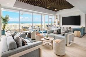A spacious living area with a large window overlooking a beach, furnished with sofas and a coffee table. - Hilton Garden Inn Ocean City Oceanfront (Ocean City)