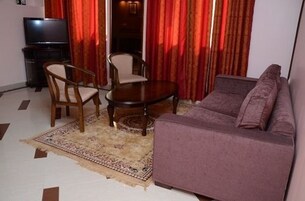 Una sala de estar con sofá, dos sillones, una mesita, televisor y cortinas rojas.