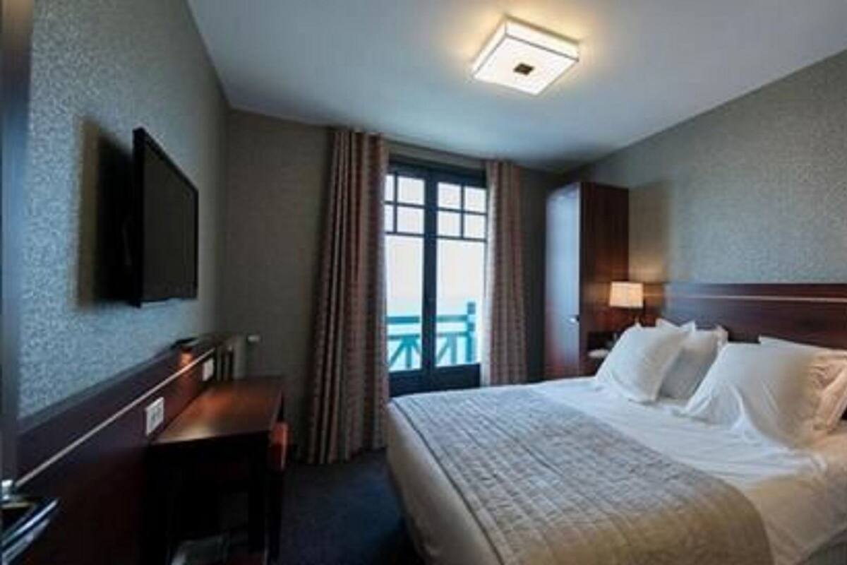 A hotel room with a large bed, bedside lamps, a flat-screen TV, a desk, and a window with curtains.