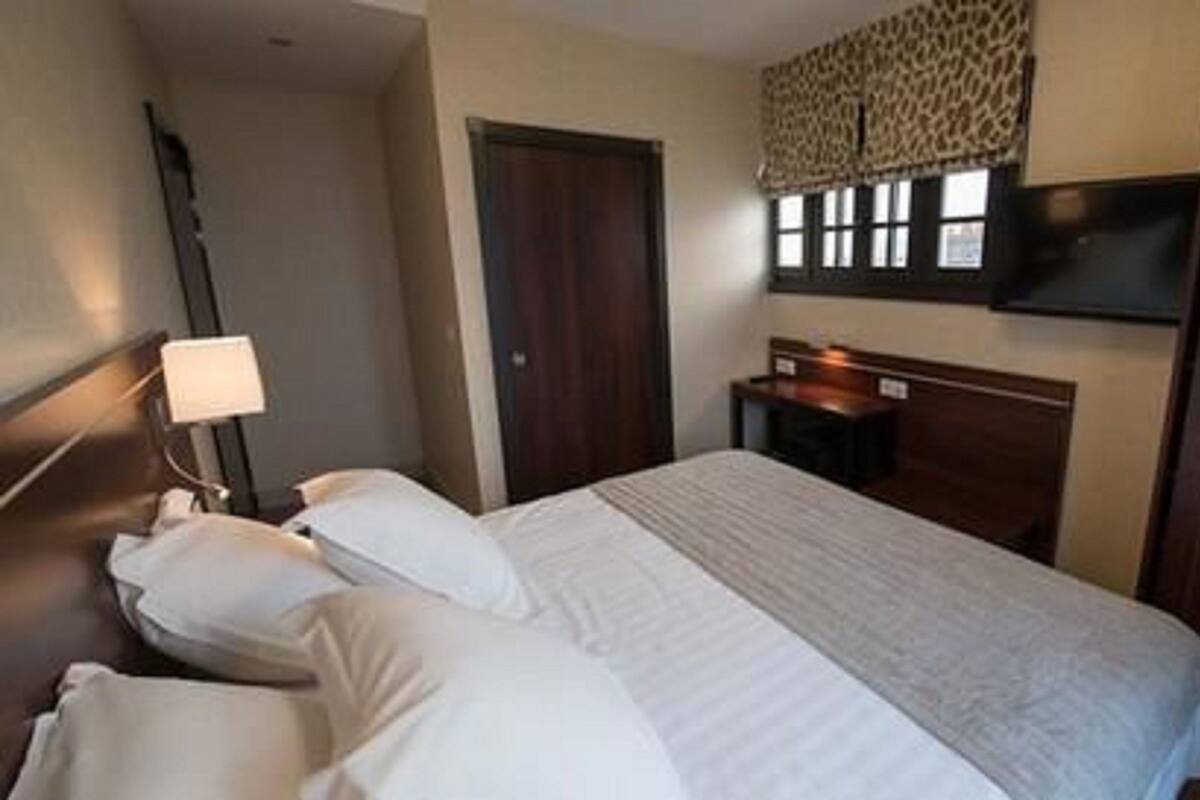 A hotel room with a bed, a desk, a lamp, and a wardrobe.