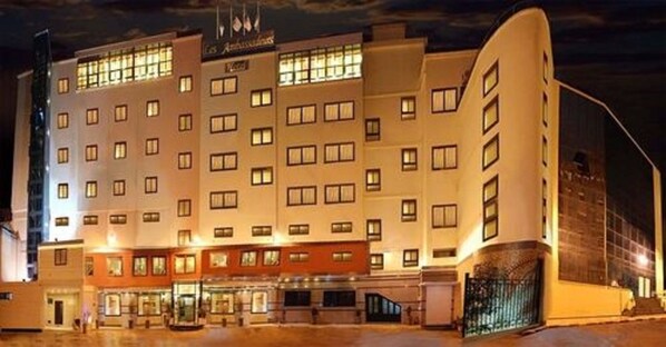 Un hotel de varios pisos con una entrada central, un área exterior cubierta y un estacionamiento.