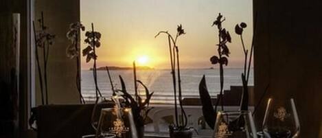 A table with a view of the sunset over the ocean, decorated with orchids and wine glasses.