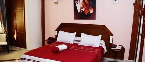 A neatly made bed with a red and white bedspread, a wooden headboard, and a nightstand with a lamp.
