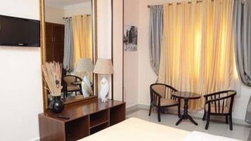 Una habitación de hotel con cama, escritorio con lámpara, silla, televisión y cortinas.