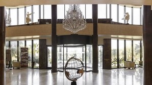 A spacious lobby with a large chandelier, a unique spherical chair, and a view of palm trees through large windows.