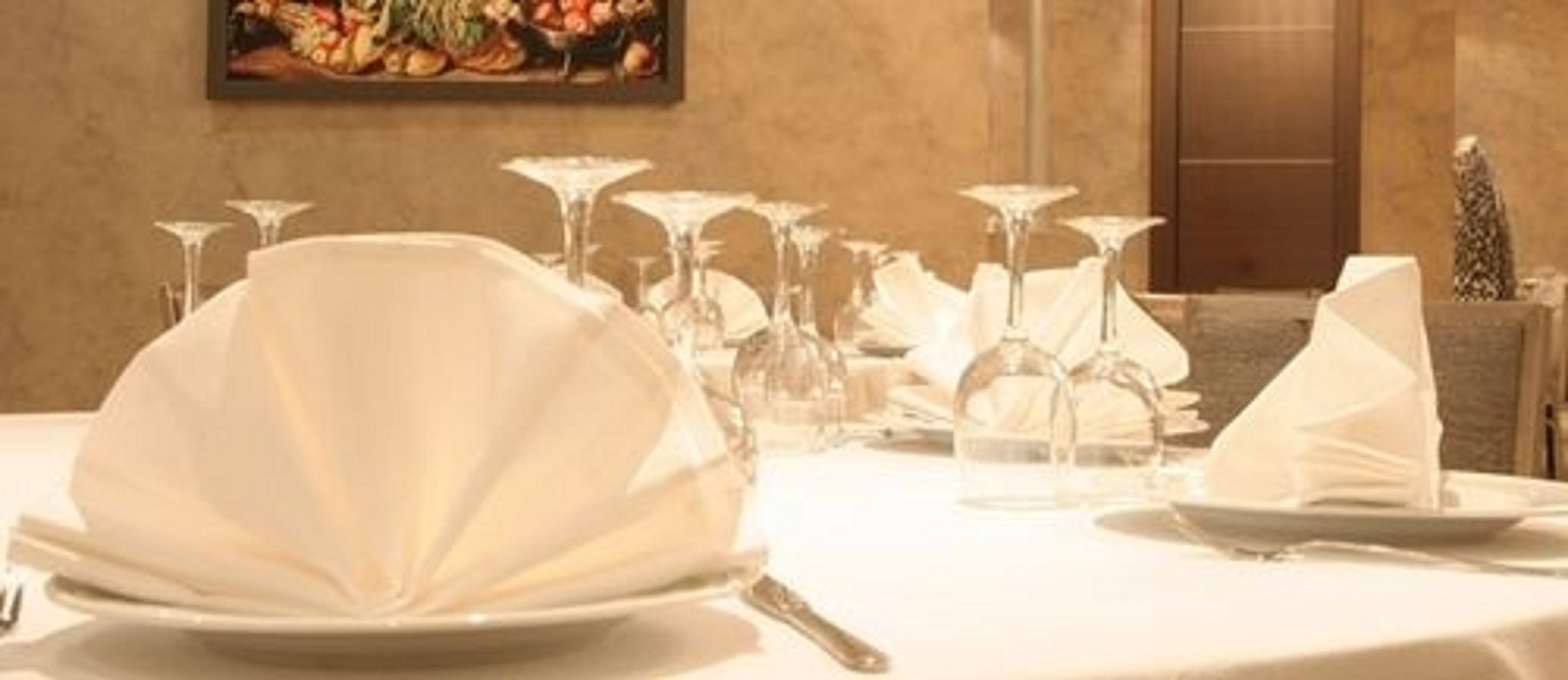A dining table set with white tableware and glassware, a painting on the wall, and a door in the background.