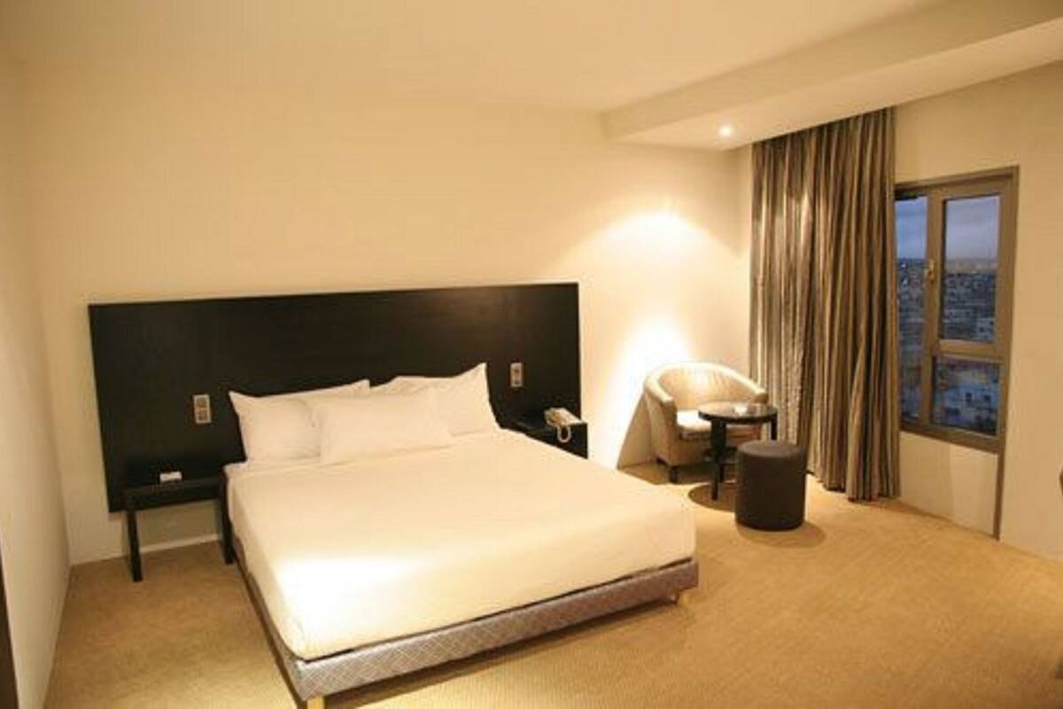 Hotelkamer met een groot bed, een stoel, een tafeltje en uitzicht op de stad.
