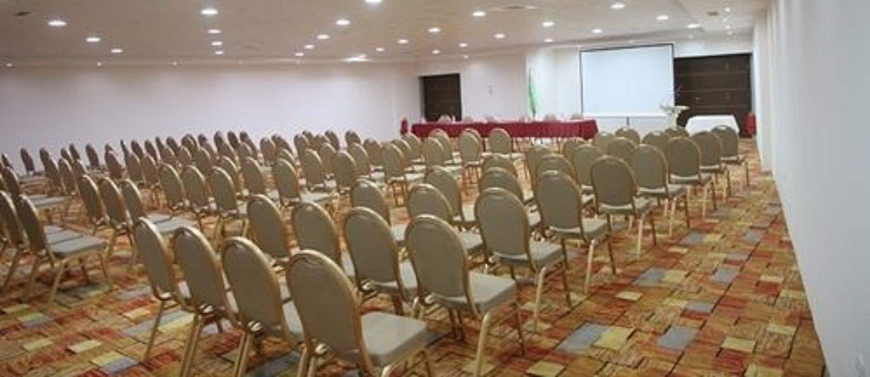 Un salón de conferencias con filas de sillas y una zona de escenario.