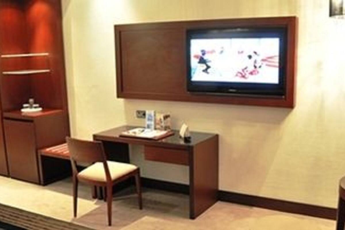 Een hotelkamer met een aan de muur bevestigde televisie, een bureau met stoel en een klein tafeltje.