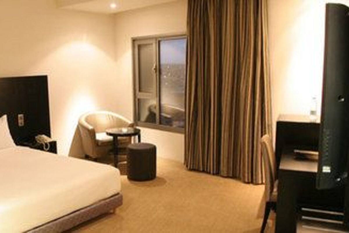 Een hotelkamer met een groot bed, een stoel, een kleine tafel, een televisie en een raam met gordijnen.
