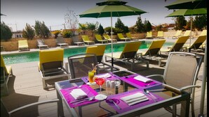 A poolside area with lounge chairs and umbrellas, a table with a drink and napkins, and a clear view of the pool.