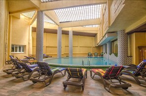 An indoor swimming pool with lounge chairs and a high ceiling with a skylight.