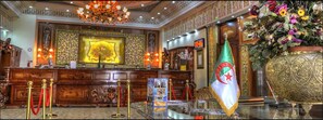 A lobby with a reception desk, a flag, and a large decorative vase. - Hotel Ville des Roses (Blida)