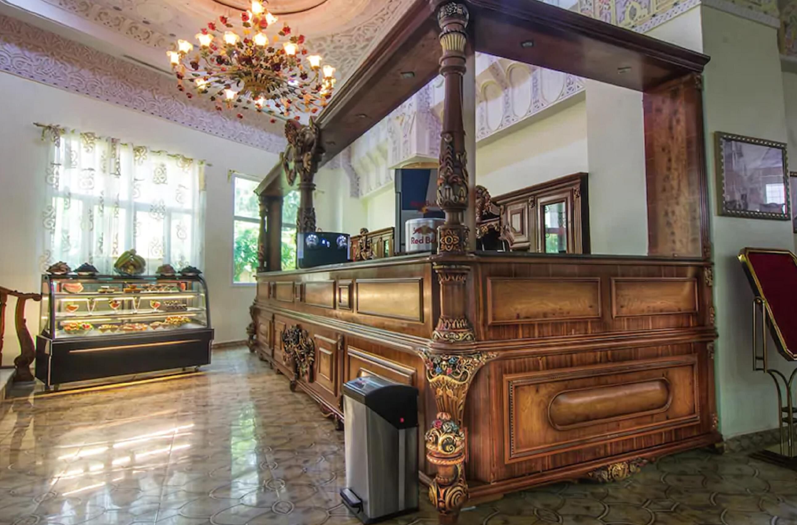 A grand room with ornate wooden furniture, a chandelier, and a display case with food items.