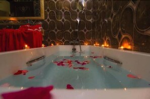 A bathtub with rose petals and candles, set against a patterned wall. - Hotel Ville des Roses (Blida)