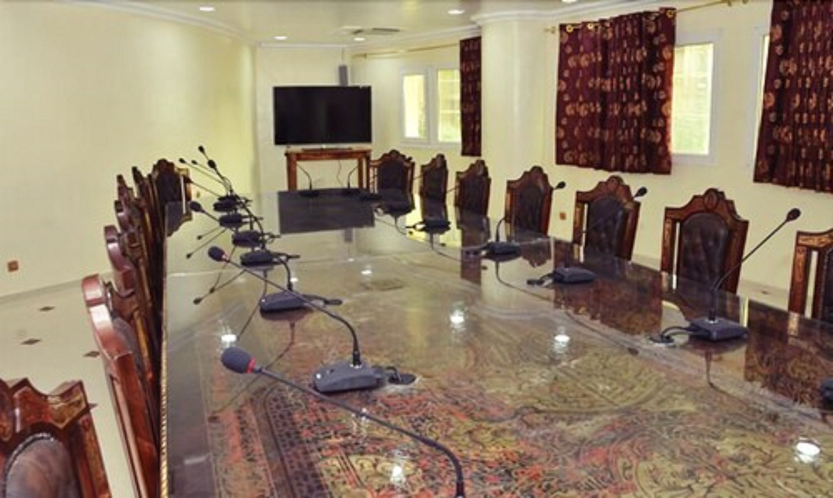 Une salle de conférence avec une longue table, des chaises, un téléviseur et une moquette à motifs.