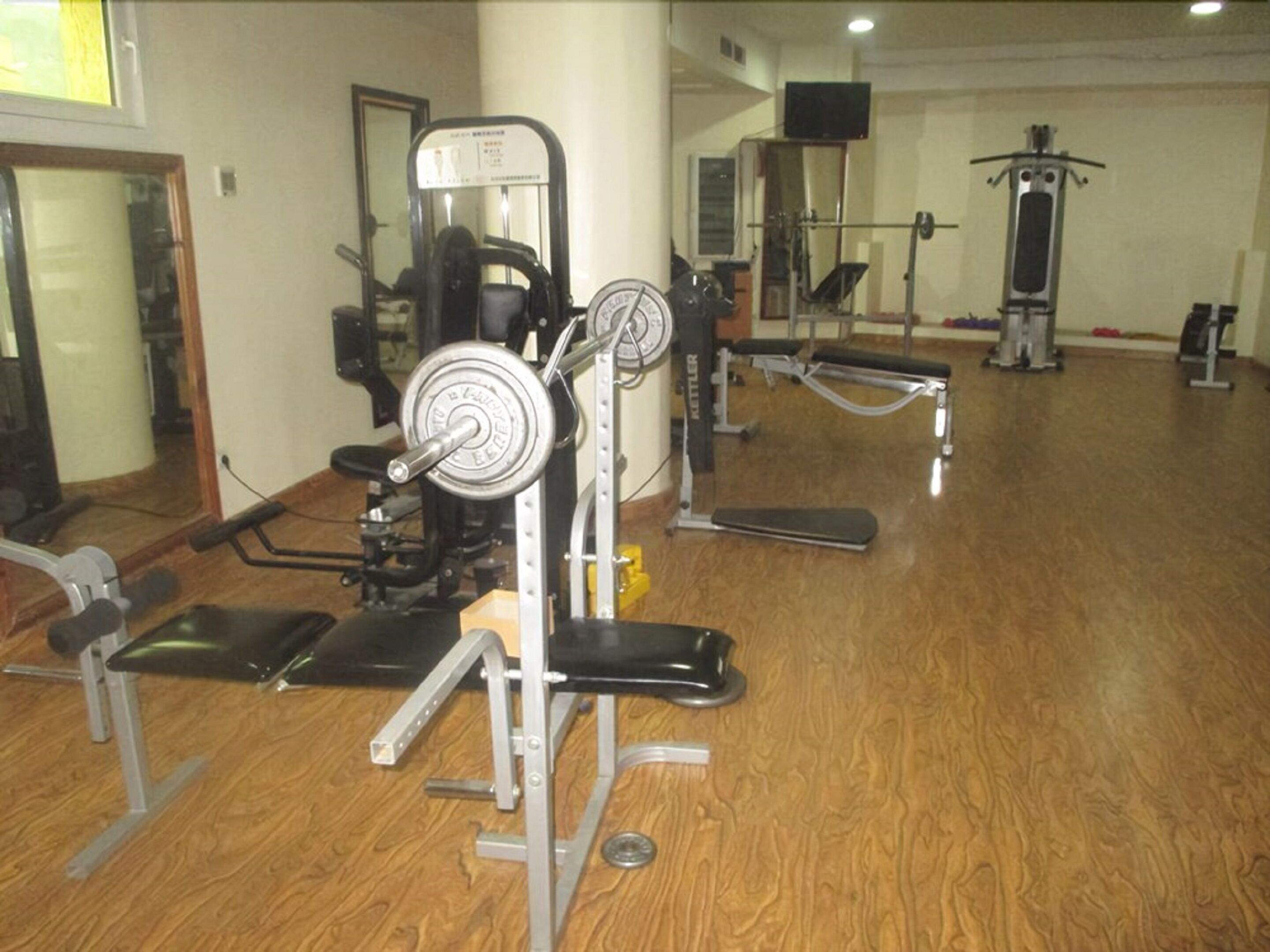 A gym with various exercise equipment, including a bench press, a squat rack, and a cable machine.