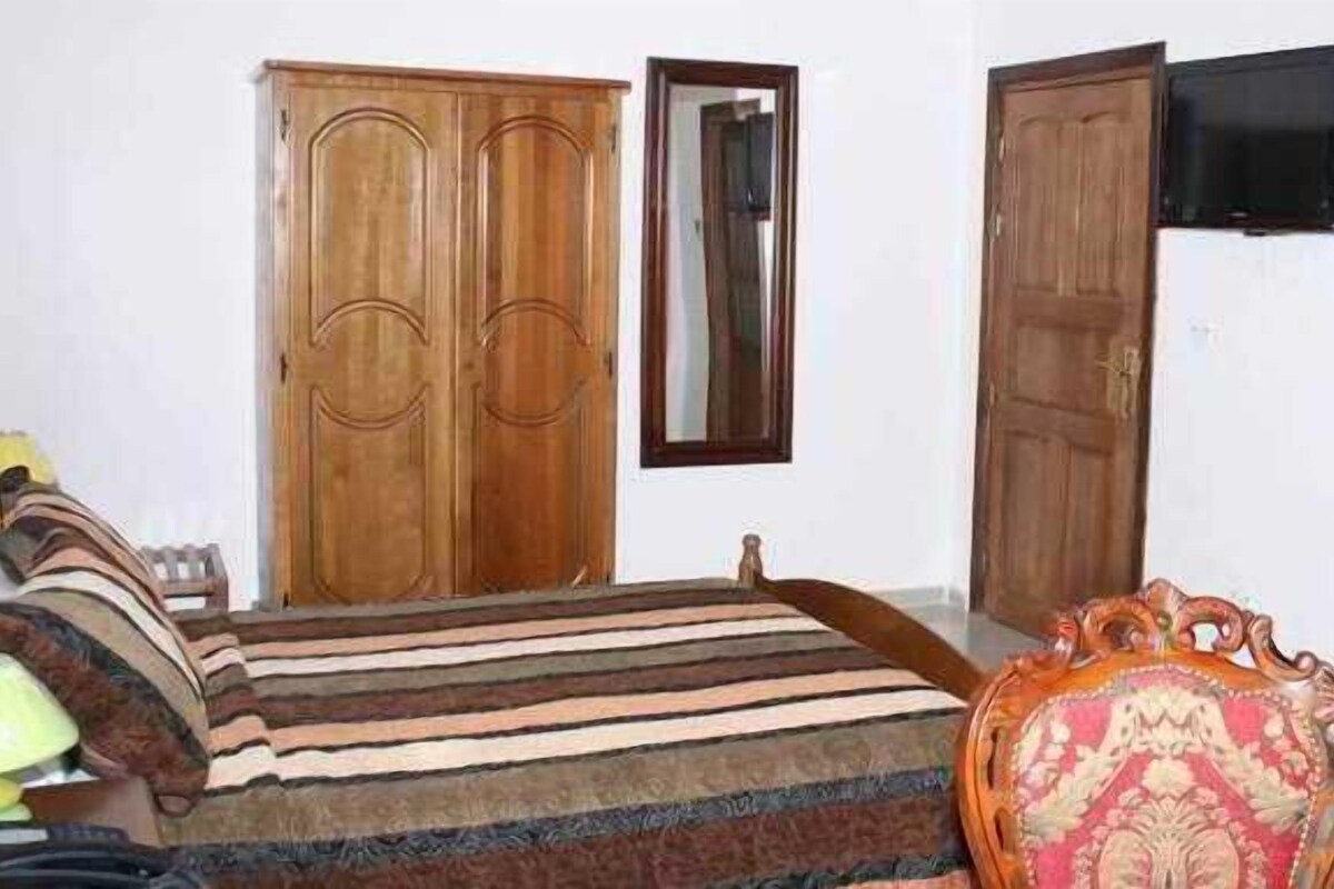 Une chambre à coucher avec un lit, une armoire, une télévision et une chaise.
